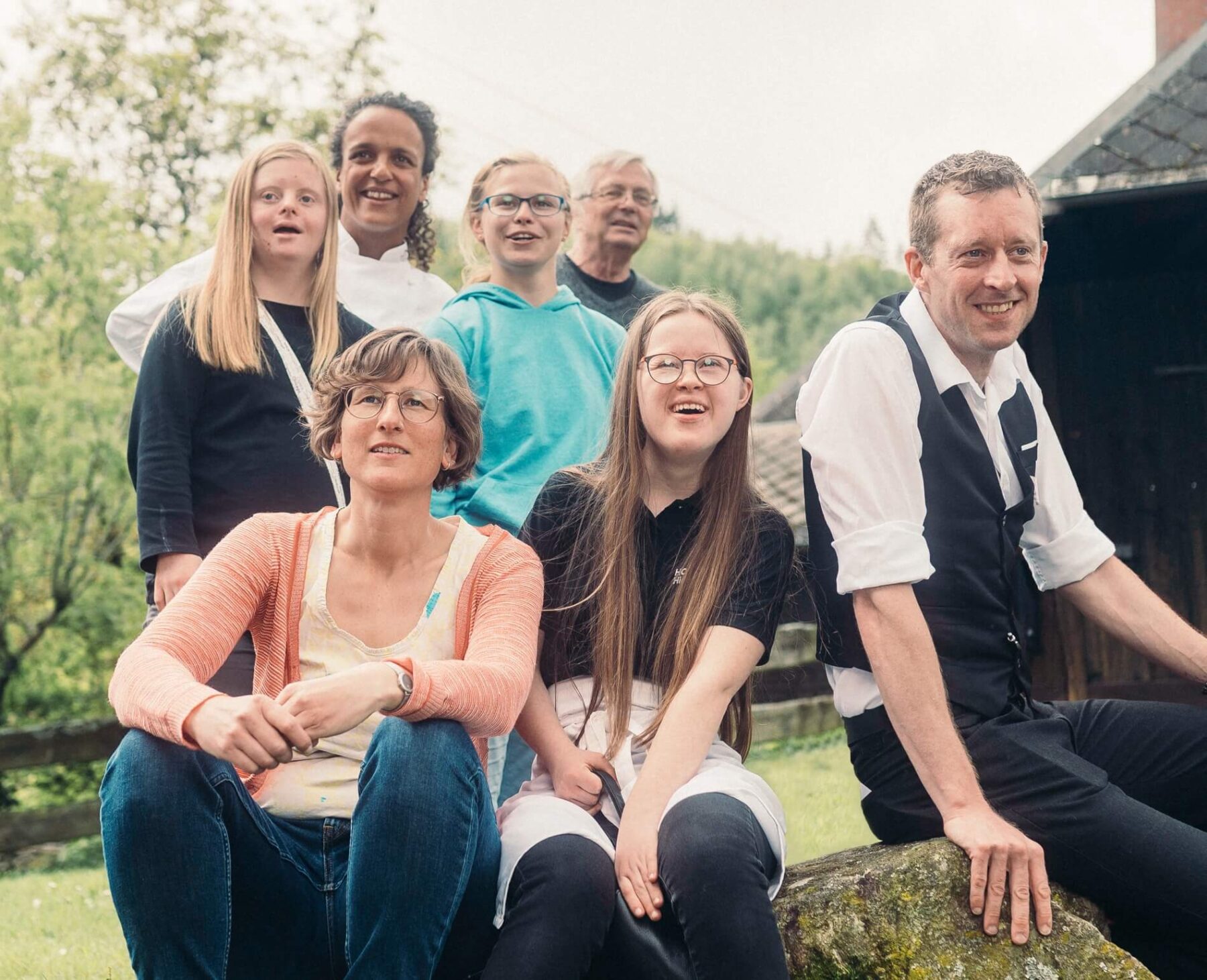 Gruppenbild mit unterschiedlichen Menschen auf einem Stein vor dem Hofgut Himmelreich