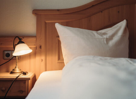 Nahaufnahme Nachtischlampe mit aufgeschlagenem Kissen und Holzbett
