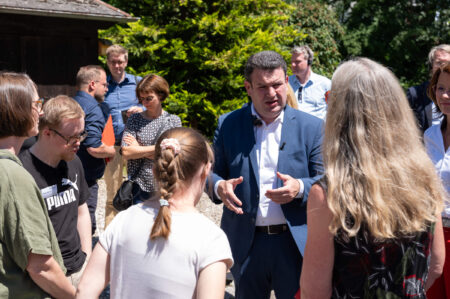 Bundesminister Hubertus Heil vorm dem Hofgut im Gespräch mit einer Teilnehmerin und ihrer Mutter. Weitere Personen stehen rund um ihn.