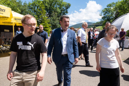 Bundeminister Hubertus Heil läuft mit zwei Teilnehmenden über den Platz vor dem Hofgut. Hinter ihnen Journalisten.