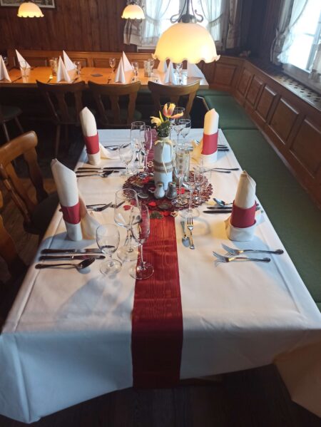 Für Valentinstag gedeckter Tisch. Rote Herzchendeko und Blumen stehen auf einer gedeckten Tafel in der Gaststube.